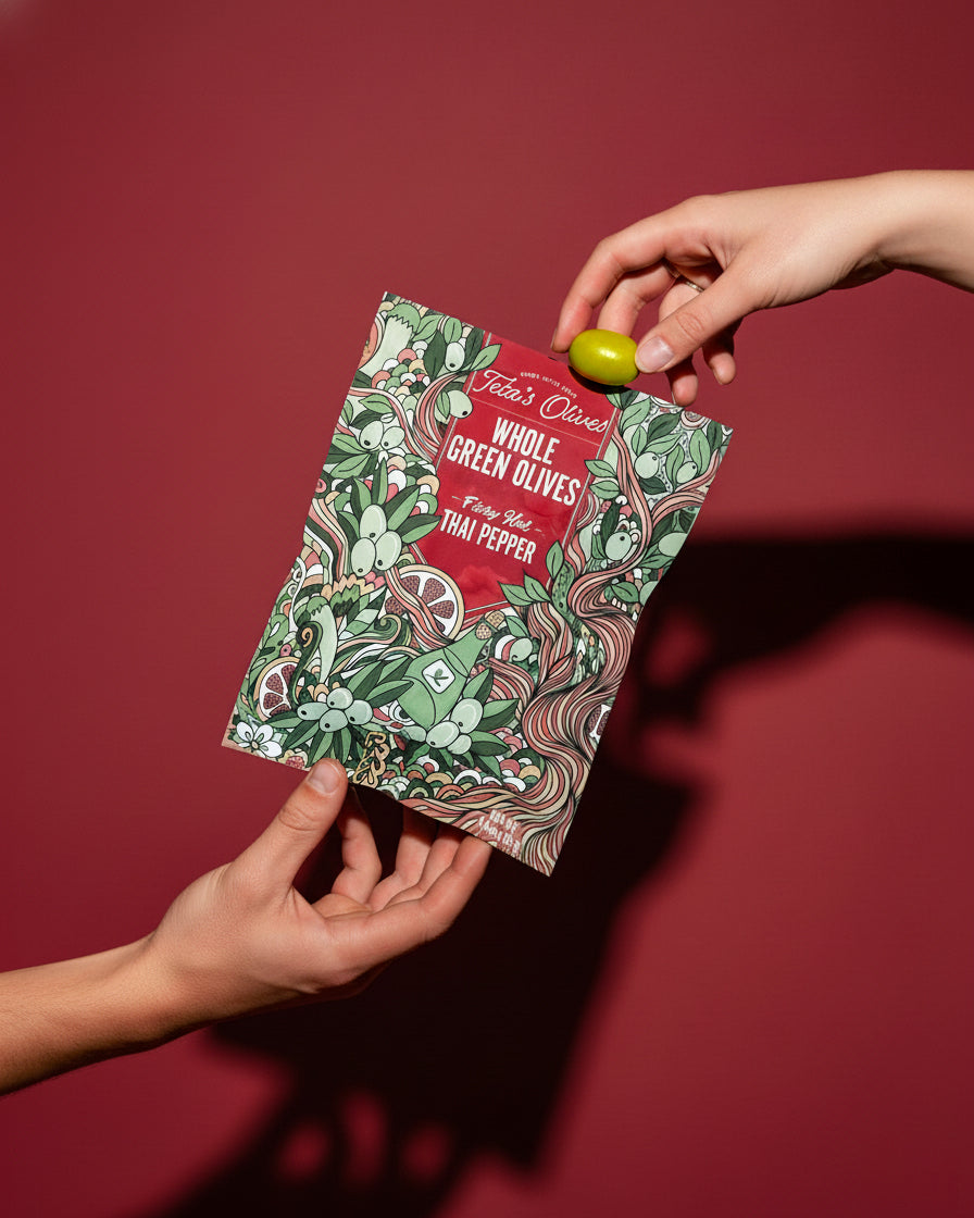 Hand holding a packet of whole green olives against a red background