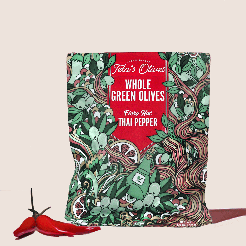 front view of teta's olives bag of fiery hot thai pepper on a granite counter, surrounded by thai peppers, pile of crushed red peppers, and a small bowl of whole green olives in the background