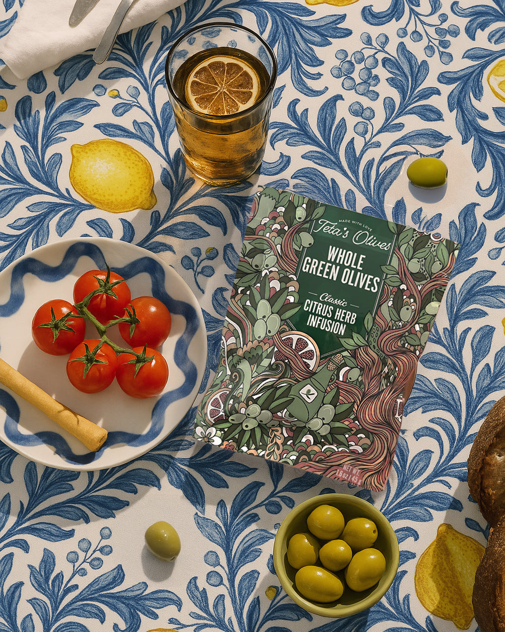 overhead image of a citrus herb bag on a table surrounded by olives, tomatoes, lemonade cup