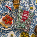 Overhead picture of Teta's Olives Thai Pepper on a table surrounded by green olives in a bowl, tomatoes, peppers, a lemonade cup