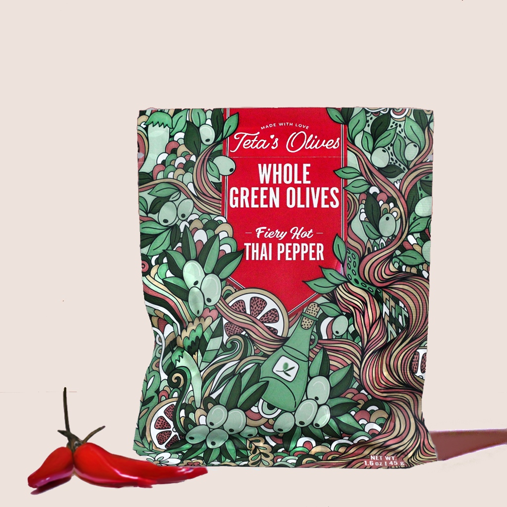 front view of teta's olives bag of fiery hot thai pepper on a granite counter, surrounded by thai peppers, pile of crushed red peppers, and a small bowl of whole green olives in the background